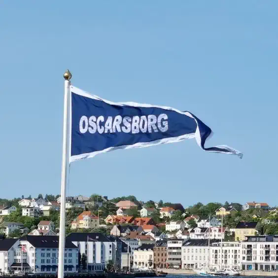 Navnevimpel med teksten Oscarsborg heist i flaggstang med arendal by i bakgrunnen