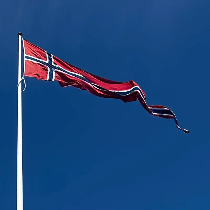 Flott norsk korsvimpel heist i flaggstang med blå himmel bak